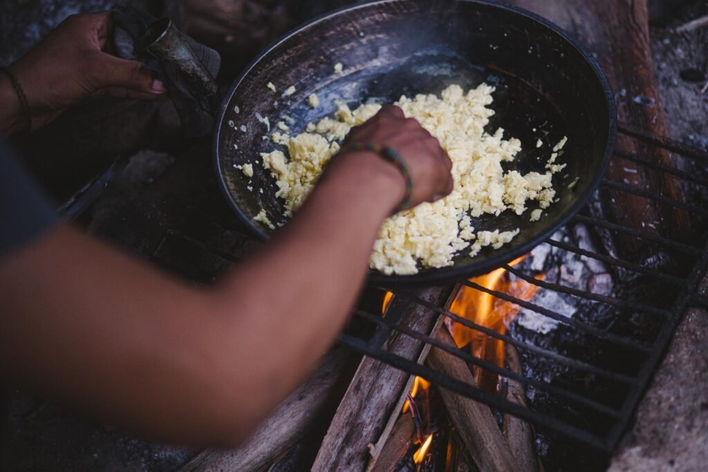 Scrambling eggs in a pan set on a grate over a campfire